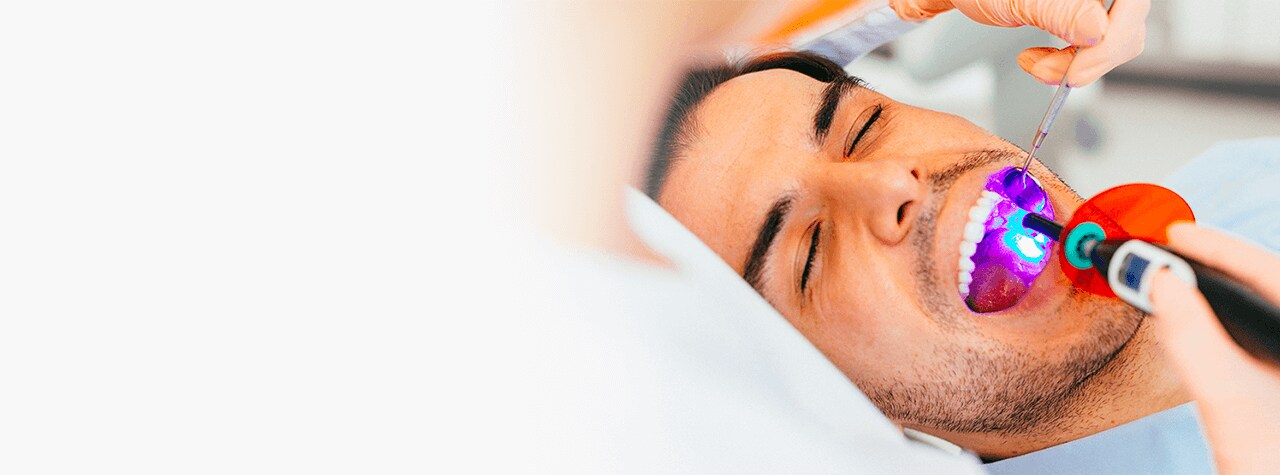 A dental professional wearing safety PPE gear and white lab coat smiling compassionately