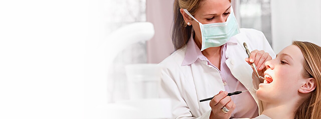A dental professional wearing safety PPE gear and white lab coat smiling compassionately