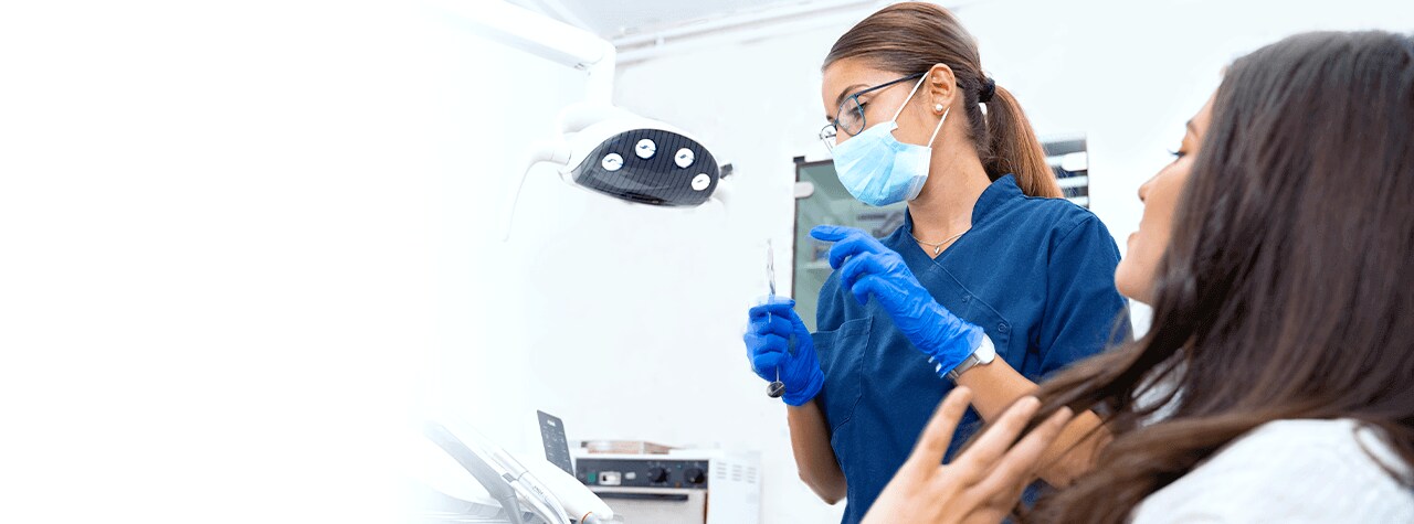 A dental professional wearing safety PPE gear and white lab coat smiling compassionately